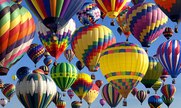 Numerous colorful hot air balloons float serenely in a clear, blue sky, creating a vibrant and mesmerizing aerial display, each balloon showcasing different patterns and hues.